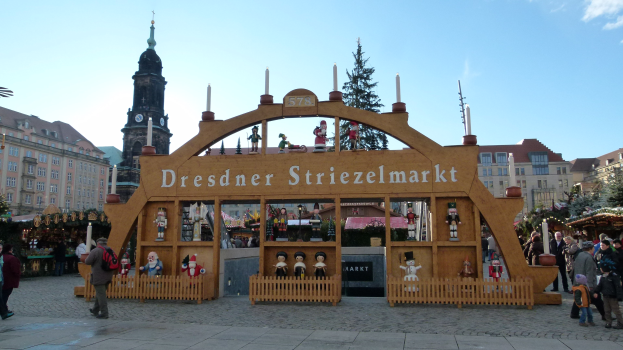 Ein belebter Weihnachtsmarkt in Dresden, Deutschland mit Menschen, einem Torbogen, Bäumen, Gebäuden und bewölktem Himmel.