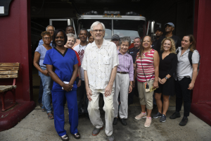 Gruppe von Freiwilligen vor einem Feuerwehrauto stehend, mit einer Bank links und einer Wand im Hintergrund.