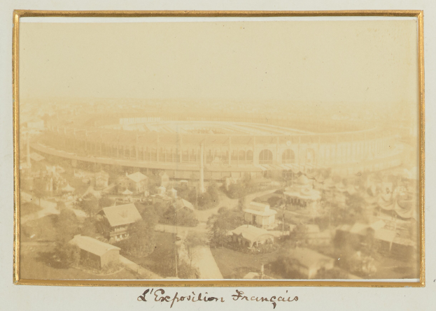 Altes Schwarz-Weiß-Foto eines Stadions inmitten einer Stadtlandschaft, umgeben von Gebäuden, Bäumen und Strommasten, mit Text am unteren Rand.