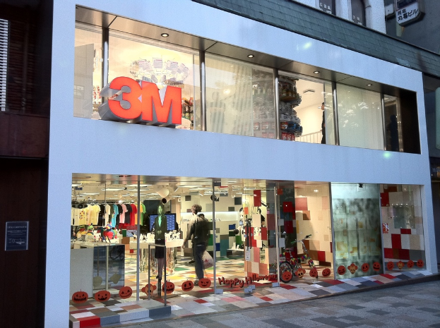 Ein Gebäude mit einer Glaswand, auf der Kleider an Bügeln, eine Schaufensterpuppe, ein Fahrrad, aufgeklebte Bilder und auf die Scheibe geschriebener Text zu sehen sind.