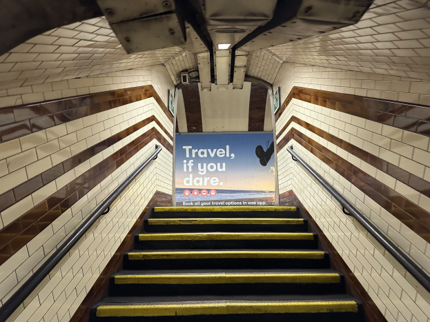 Eine Treppe in einer U-Bahn-Station mit einem "Reise, wenn du wagst"-Schild oben, flankiert von Geländern und U-Bahn-Stationswänden im Hintergrund.