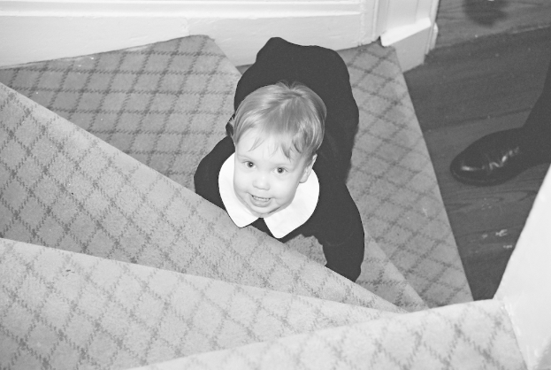 Ein Kind sitzt auf einer Treppe mit Schuhen, die rechts placed in einem Schwarz-Weiß-Bild.