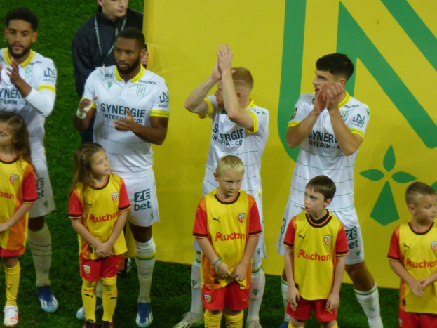 Eine Gruppe von Fußballspielern in Uniformen klatscht auf einem Ligue-1-Feld in celebration, mit einem "Ligue-1" Schild im Hintergrund.