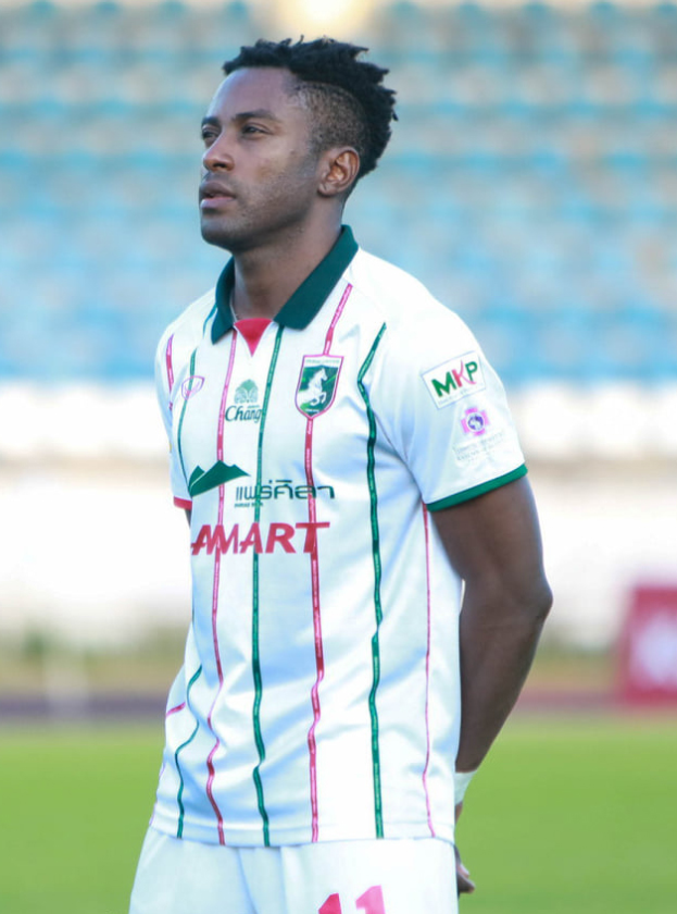 Der ghanaische Fußballspieler Emmanuel Adebayor steht auf einem Fußballfeld in einem weißen und grünen T-Shirt und Shorts und hat einen unscharfen Hintergrund.