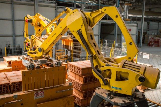 Ein großes Lager voller numerous boxes, Kräne, einen Zaun, Pfosten und andere industrielle Ausrüstung, mit einer Wand im Hintergrund.