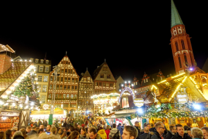 Ein geschäftiges Weihnachtsmarkt in Nürnberg, Deutschland mit Menschen um dekorierte Stände, Gebäude mit Fenstern, einen Uhrenturm und einen dunklen Himmel.