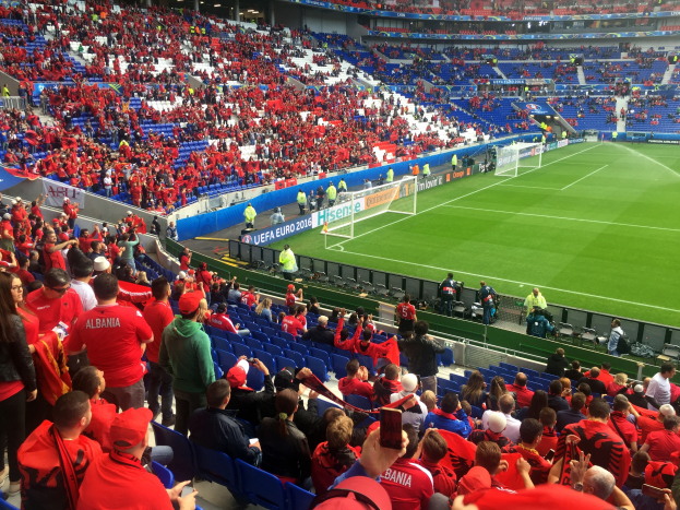 Eine große Menschenmenge in einem Stadion schaut einem Fußballspiel zu, mit Fahnen, einem Torpfosten und Deckenbeleuchtung.