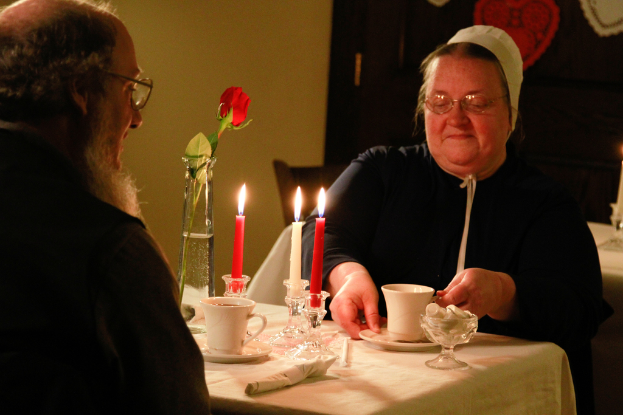 Zwei Personen an einem Tisch mit einer Tasse, Kerzen und einer Blume darauf.