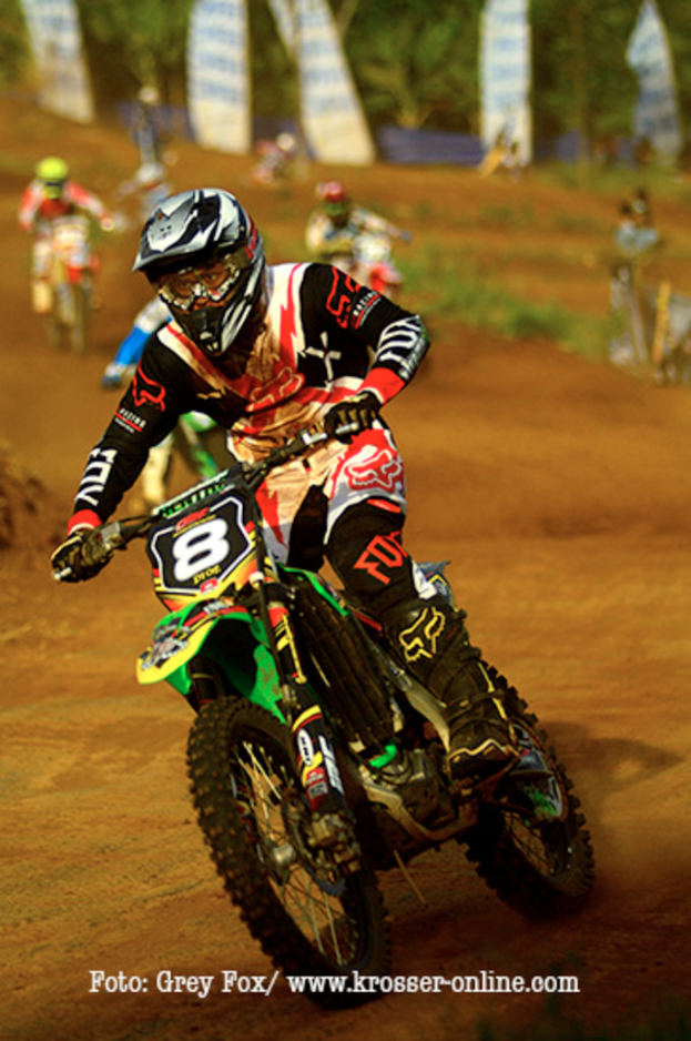 Mehrere Motorradfahrer mit Helmen nehmen an einem Rennen teil, wobei unten auf dem Bild Text angezeigt wird.