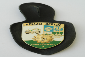 Ein Polizeistern mit der Aufschrift "Polizei Berlin" auf einem blauen Schild mit einem weißen Stern in der Mitte, umgeben von einem weißen Rand, auf einer Oberfläche.