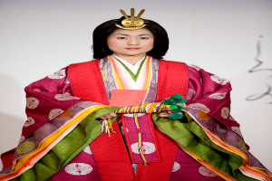 Eine Frau in einem traditionellen japanischen Kimono, das ein lebhaftes rotes und grünes Kleid mit aufwändigen Mustern trägt, steht selbstbewusst auf einem Laufsteg mit ihrem Haar zu einem ordentlichen Knoten gebunden.