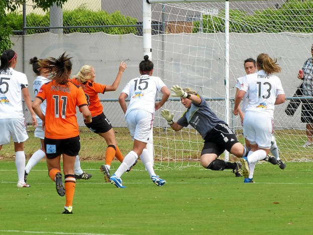 Eine Gruppe von Frauen, die auf dem Rasen ein Spiel spielen, im Hintergrund ein Maschendrahtzaun und Bäume.