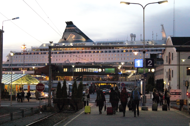 Eine Gruppe von Menschen, die auf einer Straße gehen und Taschen tragen, mit Polen und Gebäuden im Hintergrund.