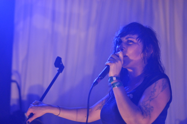 Eine Frau mit Tätowierungen an den Händen singt in ein Mikrofon.