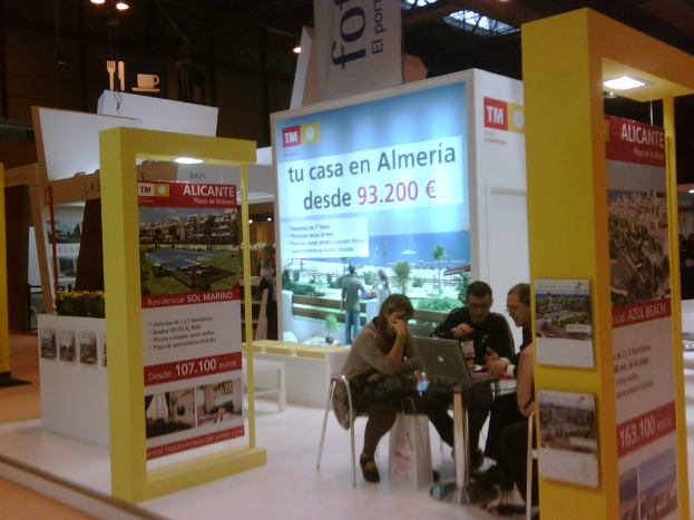 Eine Gruppe von Menschen, die um einen Tisch sitzen und auf einen Laptop schauen, mit mehreren Flyern mit verschiedenen Werbeanzeigen daneben.