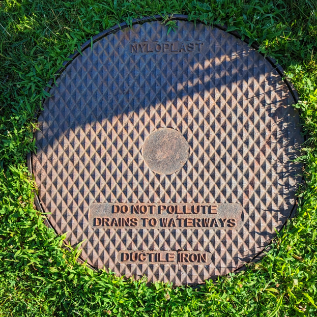 Ein Gullydeckel im Gras mit der Aufschrift "Verunreinigen Sie keine Abflüsse in Gewässer"