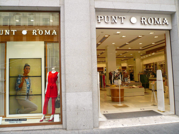 Vorderseite von Punt Roma in Mailand, Italien, mit Schaufensterpuppen in Fensterkleidung, beleuchteter Decke, Wandtext und einer Fußmatte auf dem Boden.