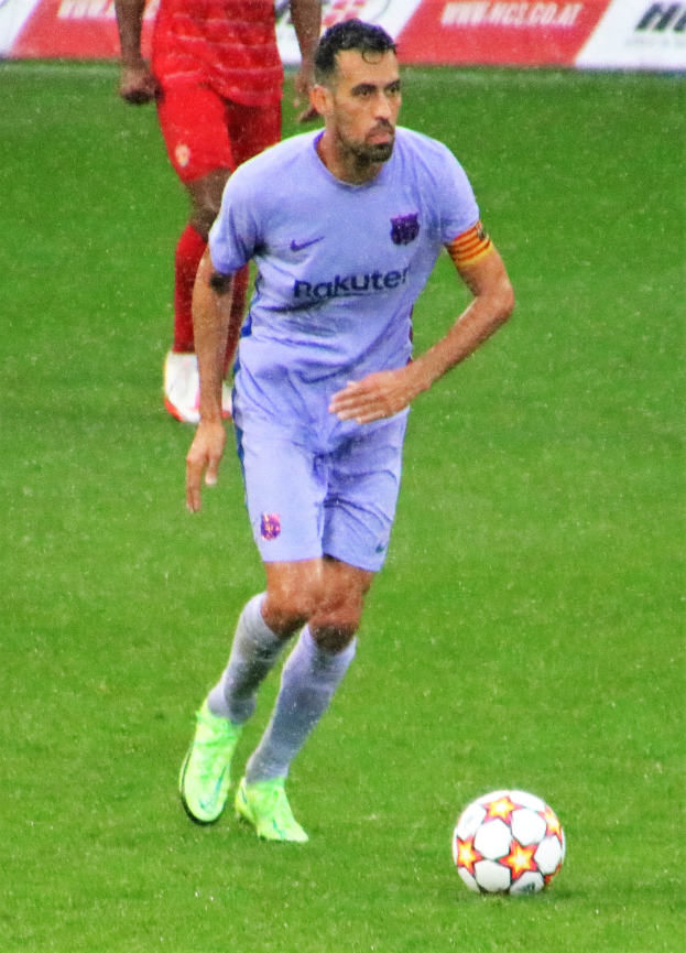 Ein Fussballspieler in Sportbekleidung und -schuhen ist im Einsatz auf dem Feld, mit einer Texttafel im Hintergrund.