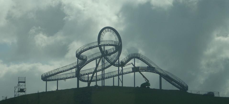 Eine Achterbahn auf dem Gipfel eines Hügels unter einem bewölkten Himmel, umgeben von Stützpfählen und -strukturen.