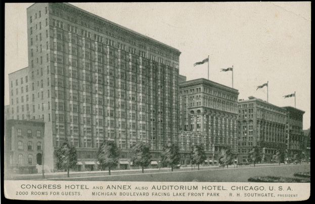Ein Schwarz-Weiß-Foto des Congress-Hotels und des Annex Auditorium Hotels in Chicago, Illinois, ein großes Gebäude mit vielen Fenstern, umgeben von Bäumen und Fahnenstangen, mit einem klaren Himmel im Hintergrund und Text am unteren Rand des Bildes.