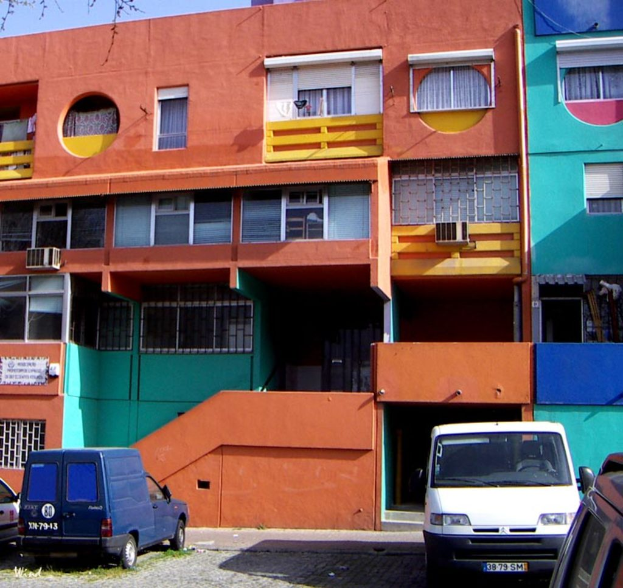 Eine Szene mit mehreren Gebäuden, einem Zaun, mehreren Fahrzeugen und einem Himmel.