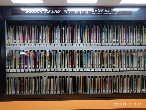 Eine gut beleuchtete Bibliothek mit hohen Bücherregalen voller Bücher, ein sichtbares Textbrett und ein Wasserzeichen unten, das an eine Selbstbedienungsbibliothek in einer städtischen Umgebung erinnert.