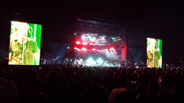 Eine Konzertszene mit einer Menge unten und einem großen Bildschirm links sowie einem kleineren Bildschirm rechts.