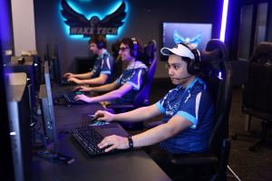 Gruppe von Menschen mit Headsets, die ein Spiel auf Computern in einem Raum spielen, der als "Wake Tech Esports" beschriftet ist