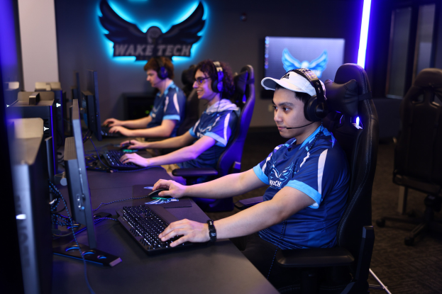 Gruppe von Menschen mit Headsets, die ein Spiel auf Computern in einem Raum spielen, der als "Wake Tech Esports" beschriftet ist