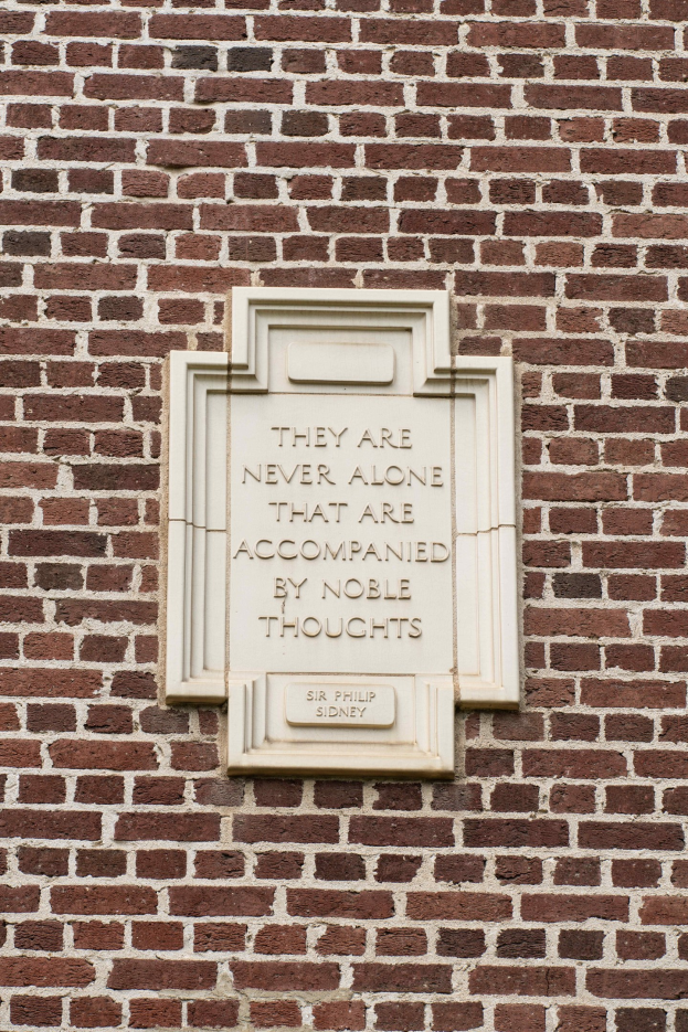 Steintafel auf einer Ziegelwand mit der eingravierten Inschrift "Sie sind nie allein, die von edlen Gedanken begleitet sind".