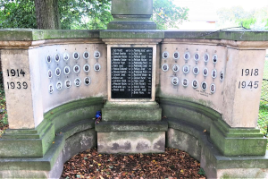 Ein Denkmal in einem von Bäumen und einem Zaun umgebenen Park mit einer Tafel an der Wand und trockenen Blättern auf dem Boden, das sich auf dem jüdischen Friedhof in Berlin befindet und als Gedenkstätte für Holocaust-Opfer dient.