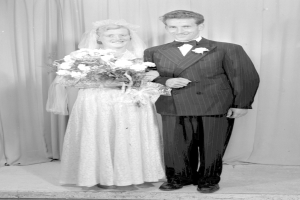 Ein Mann und eine Frau stehen nebeneinander auf einer Bühne, lächeln und die Frau hält einen Blumenstrauß, und ein Vorhang dahinter.