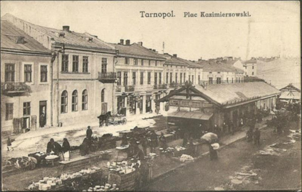 Schwarz-weiß-Foto eines vollen Marktes in Tarnopol, Polen mit Menschen auf Karren und Gebäuden im Hintergrund.