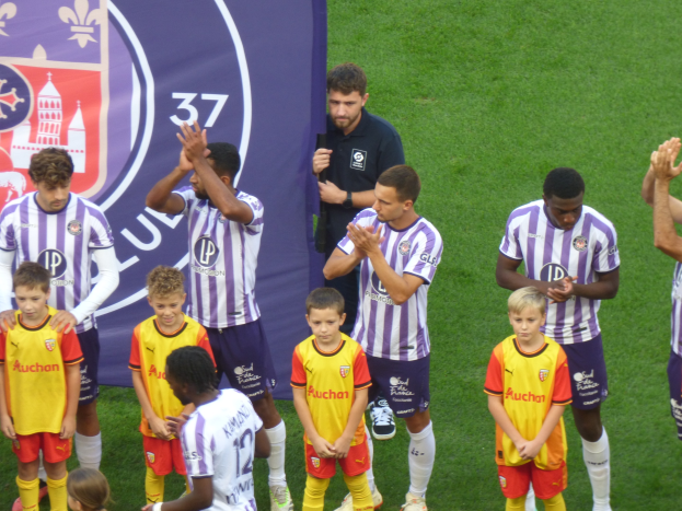 Gruppe junger Jungs, die auf einem Fußballfeld klatschen, mit einem Banner und Logos im Hintergrund.