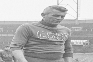 Ein Schwarz-Weiß-Foto eines Mannes, der auf einem Feld steht und ein T-Shirt mit Text trägt, vor einem Stadion und einer Werbetafel, mutmaßlich der Fußballspieler César Azpilicueta.