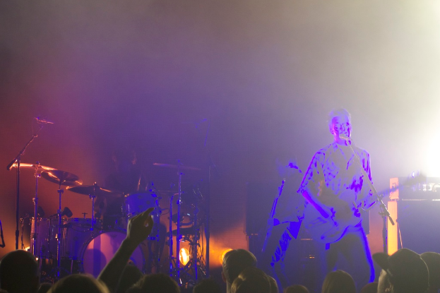 Ein Mann spielt Gitarre vor einem Mikrofon mit Musikinstrumenten und Lichtern im Hintergrund.