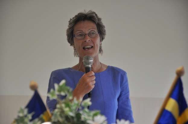 Eine Frau steht an einem Podium mit zwei Flaggen hinter ihr und spricht in ein Mikrofon.