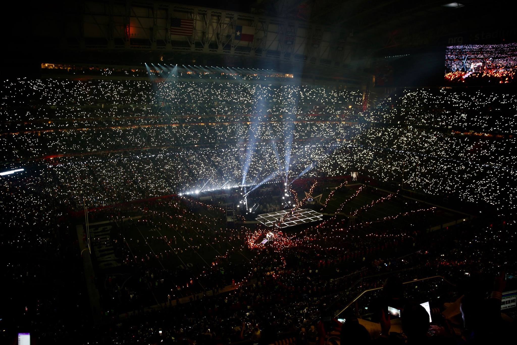 Große Menschenmenge in einem hell erleuchteten Stadion bei Nacht mit einem Bildschirm, der links die Ergebnisse der Super Bowl XLVII-Halbzeitshow anzeigt.