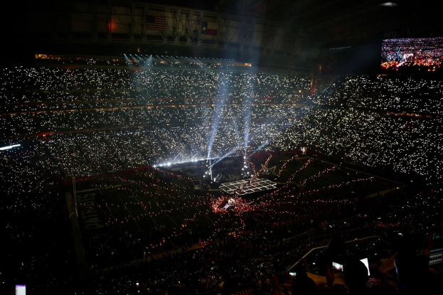 Große Menschenmenge in einem hell erleuchteten Stadion bei Nacht mit einem Bildschirm, der links die Ergebnisse der Super Bowl XLVII-Halbzeitshow anzeigt.