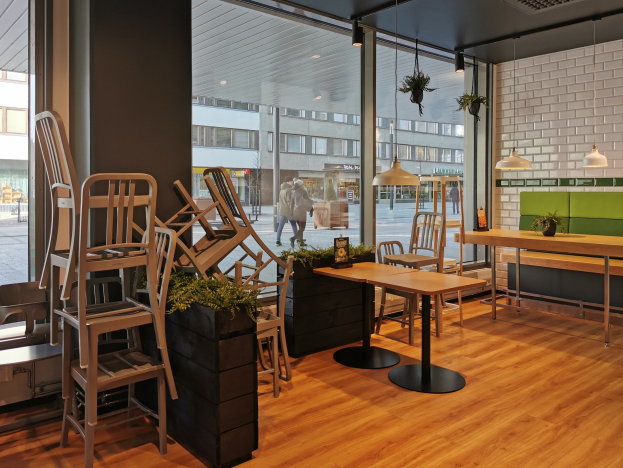 Ein Berliner Restaurant mit Holztischen und -stühlen vor einem großen Fenster, das Straßenansichten einschließlich Fußgängern, Gebäuden und städtischen Elementen zeigt.