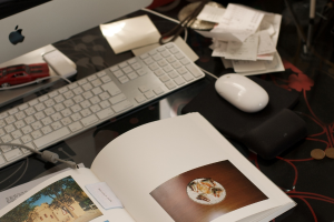 Ein Schreibtisch mit einem Monitor, einer Tastatur, einem Buch, Papieren, einer Maus, Münzen und einem Spielzeugauto.