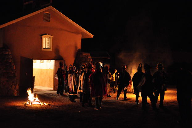 Ein Haus in der Nacht mit ein paar Menschen, die sich um ein Feuer versammelt haben.