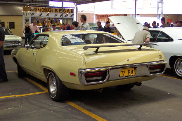 Ein Oldtimer fahrt mit Menschen in der N├Ąhe, Gesch├Ąften und Geb├Ąuden im Hintergrund.